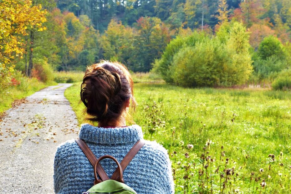 dziewczyna z plecakiem idąca polną drogą wśród drzew i krzewów